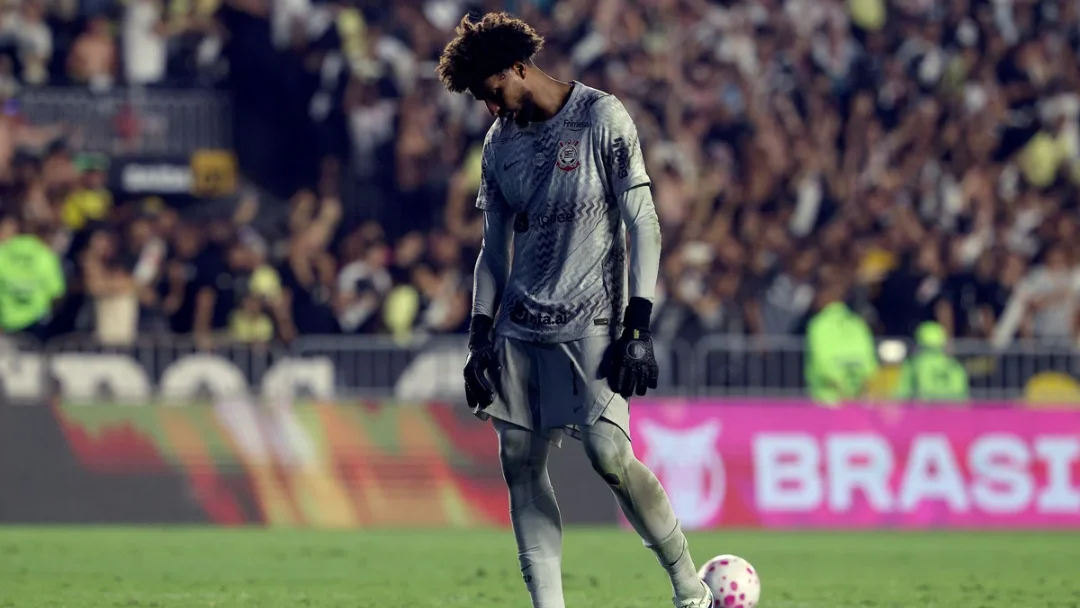 Goleiro Hugo Souza, do Corinthians, caminha de cabeça baixa pelo gramado com bola de futebol à frente